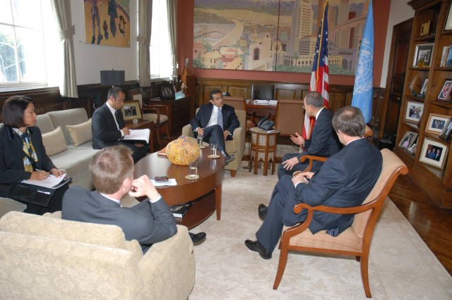 Four men and one woman in business suits sit around a coffee table in discussion with the mayor sitting in front of the desk in his office.
